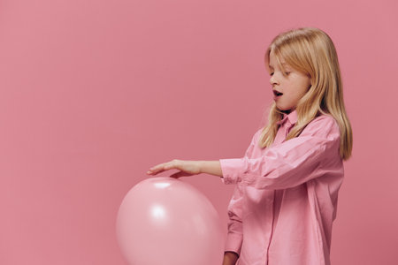 a beautiful, happy girl in a pink shirt stands on a pink background and smiling broadly at the camera holds a pink balloon in her handの写真素材