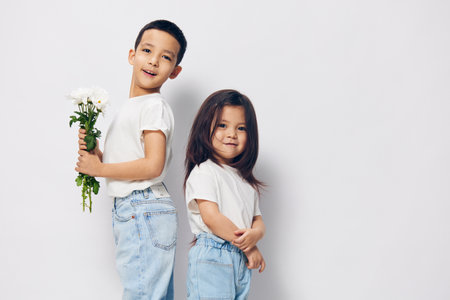 cute, happy brother and sister are standing in white clothes sideways to the camera and the boy is holding a bouquet of daisies in his hands. Themes of friendship and relationships between childrenの写真素材