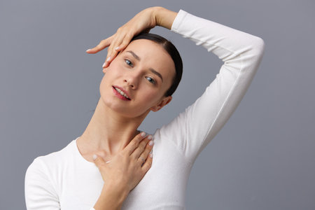 a beautiful, slender, elegant woman stands on a gray background in a white T-shirt with long sleeves...
