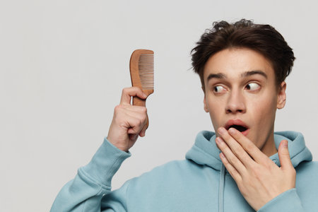 a well-groomed surprised young man in a light light blue hoodie, with a comb in his hand combing a place in the background for inserting an advertising layout.Horizontal portrait photo .の写真素材