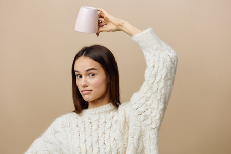funny, funny woman is standing in a white sweater turning an empty cup on her headの写真素材