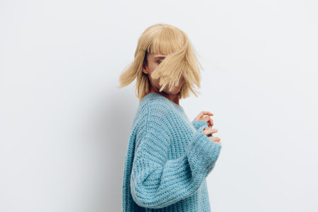 a cheerful woman in a stylish blue sweater poses on a white background and her hair falls on her face covering itの写真素材