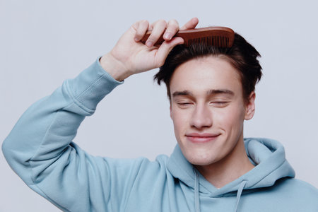 Horizontal portrait photo .a good-looking young man in a light light blue hoodie, combs his head with a comb place in the background to insert an advertising layoutの写真素材