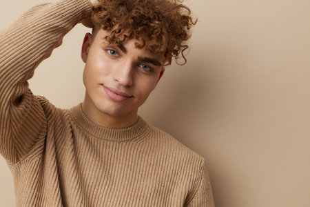 a handsome, attractive man with curly hair, in stylish clothes stands on a beige background and...