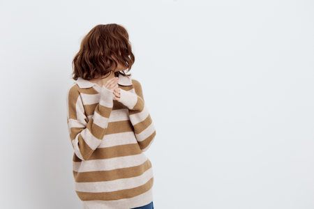 a beautiful, pleasant woman stands in a stylish striped sweater on a light background and her hair...