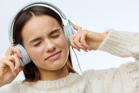 a close photo of a pleasant, sweet, attractive woman listening to music with headphones, closing her...
