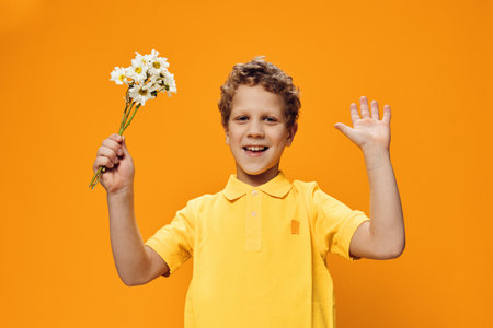 a funny, boy of school age stands in a yellow polo with a bouquet of daisies and raises his hands...
