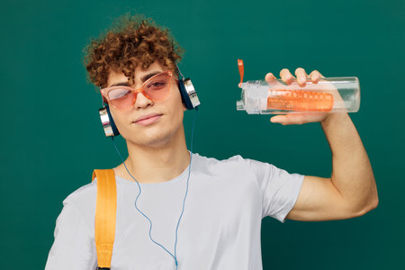 a man in gray clothes stands listening to music in headphones with bright glasses on his face, and...