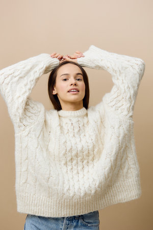 an elegant woman stands on a light background in a white sweater, raises her hands over her naked, puts them behind her back and turns her body in different directionsの写真素材