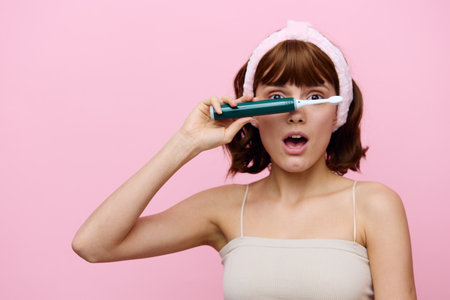 A lovely woman with clean skin, a white smile and dark beautiful hair stands on a pink background with a beautiful bandage on her head brushing her teeth.Horizontal studio shot.の写真素材