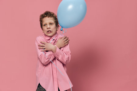 cute school age boy standing holding a blue balloon and crossing his arms over his chestの写真素材