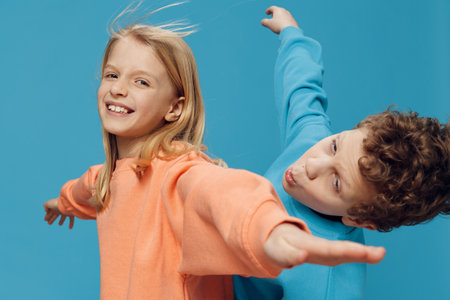 cute, beautiful children are standing on a blue background with an empty space for an advertising insert in bright clothes, sideways to the camera and stretching their arms to the sidesの写真素材