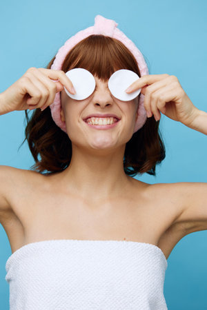 a funny, happy woman stands on a blue background smiling happily and holds a cotton pad in place of her eyesの写真素材