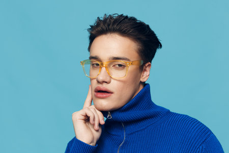 a cute, handsome man stands on a light blue background in a blue zip-up sweater and looks pleasantly...