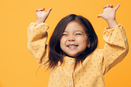 a cute, joyful preschool girl stands on an orange background and dances happily in a beautiful...