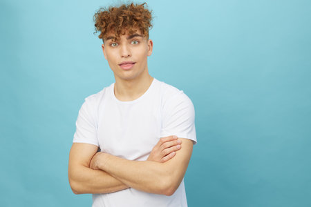 an attractive man with curly hair stands on a light blue background in a white cotton T-shirt and...