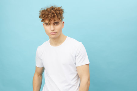 horizontal isolated portrait of a handsome man with curly hair smiling pleasantly at the camera while standing in a casual white T-shirtの写真素材