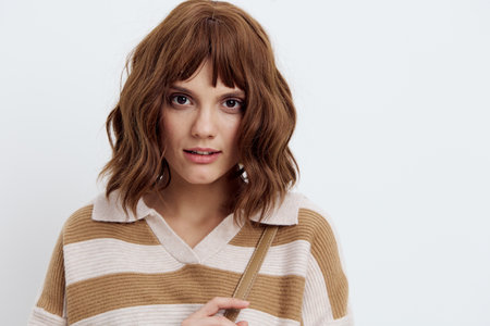 a beautiful, pleasant woman in a striped sweater looks at the camera standing on a white backgroundの写真素材