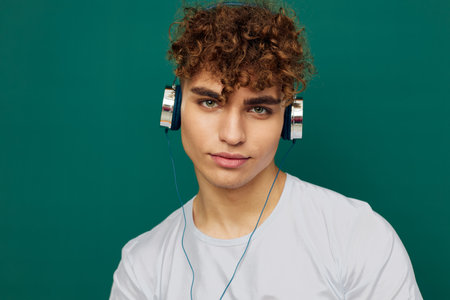 a close horizontal portrait of a handsome man with curly hair standing on a green background listening to music with headphones.の写真素材