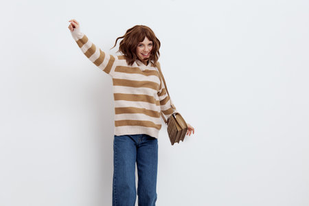 a joyful, funny woman vigorously rubs her hand up, in stylish clothes, standing on a white background holding a beige bag on her shoulderの写真素材
