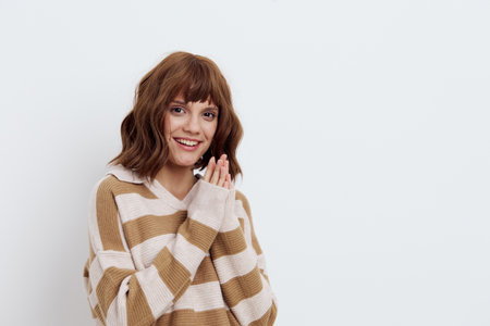 a beautiful, pleasant, emotional woman in a striped sweater looks into the camera smiling broadly, standing on a white background and holding her hands together in a relaxed gestureの写真素材