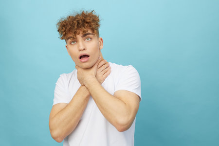 an emotional, crazy man stands on a light blue background and strangles himself with his handsの写真素材