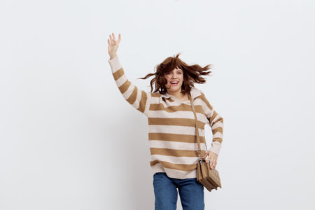 a joyful, funny woman vigorously rubs her hand up, in stylish clothes, standing on a white background holding a beige bag on her shoulderの写真素材