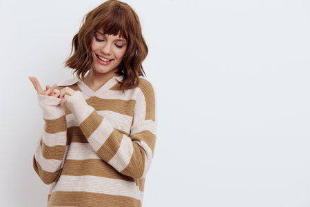 a beautiful, pleasant, emotional woman in a striped sweater looks away standing on a white background and holds her hands together in a relaxed gestureの写真素材