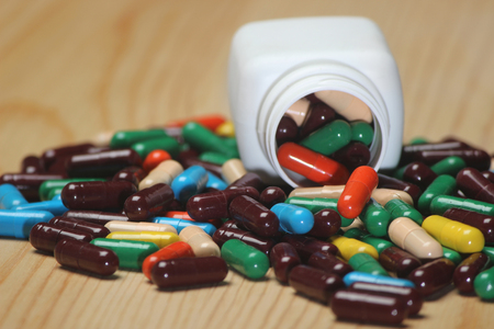 Closeup of capsules isolated on wooden background. Pills can contain any medicine, herbal or chemical. White bottle used for product packing medicine.の写真素材