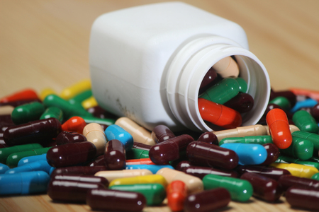 Closeup of  colorful capsule pills isolated on wooden background. Pills can contain any medicine, herbal or chemical. White bottle used for product packing medicine.の写真素材