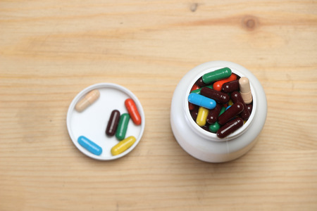 Colorful capsules bottle with lid  isolated on wooden background. Pills can contain any medicine, herbal or chemical. Product packing medicine.の写真素材