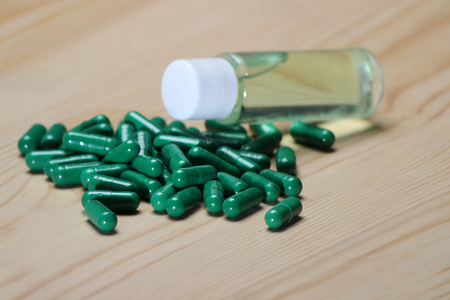 Green vitamin capsule with glass herbal oil bottle on wooden background.の写真素材