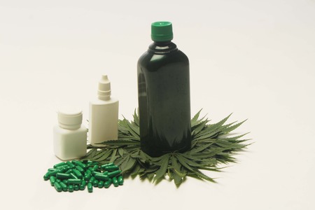 Decoration of marijuana leaves below ayurvedic medicine bottle. Ayurvedic green tablets ,white medicine bottles. Isolated on white background.の写真素材