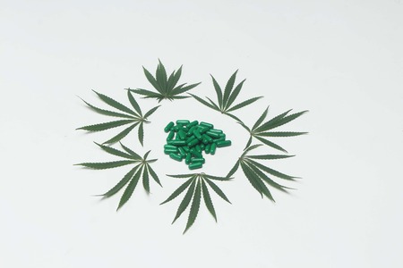 Decoration of marijuana leaves and heap of green tablets. Isolated on white background.の写真素材
