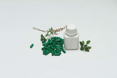 Ayurvedic green vitamin capsule, white bottle and basil leaves.Isolated on white background.の写真素材