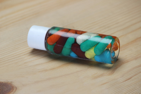 Ayurvedic capsule in glass bottle with liquid on wooden background.