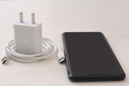 Picture of smartphone, adapter and USB cable. Isolated on wooden background.