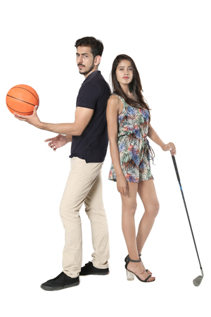 Young boy and girl opposite each other with golf stick and basketball in hand.の写真素材