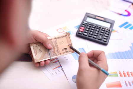 Man is holding Indian currency notes and pencil in hand.