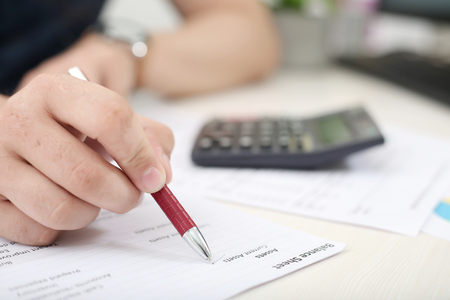 Man hand is checking balance sheet with pen.