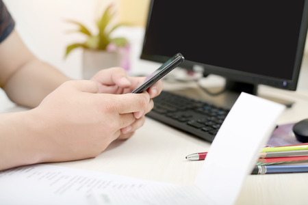 Man is using smartphone in hand. Picture of notepad, pencil, keyboard, computer, pencil and pen on...