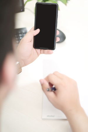 Man is using phone in one hand and other hand holding pen.の写真素材