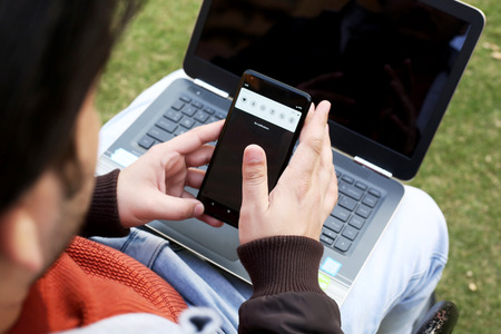 Man is working on the smartphone with laptop.