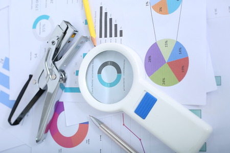 Portrait of pen, stapler, pencil and magnifying glass on the financial paper.