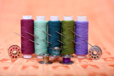 Picture of multicolored thread, bobbins and needles on the orange cloth.