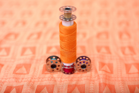Portrait of one sewing thread and bobbin on the orange cloth.の写真素材