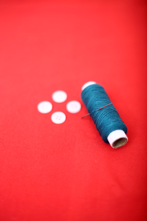 Portrait of one sewing thread with needle and button. Isolated on the red background.