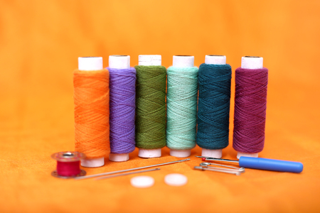 Photo of multicolored thread, needle, bobbin, button, safety pin and needle ripper. Isolated on the yellow background.の写真素材