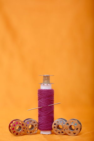 Photo of one pink sewing thread and bobbins. Isolated on the yellow background.の写真素材