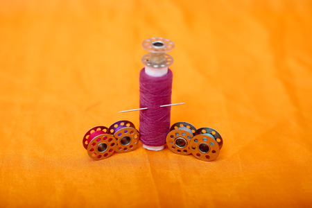 Portrait of one pink sewing thread and bobbins. Isolated on the yellow background.